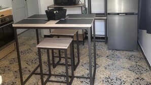 A compact kitchen with a microwave, a stainless steel refrigerator, a small table with benches, and a shelf with jars. - T2 in charming Ardèchois village (SAINT-JULIEN-EN-SAINT-ALBAN)