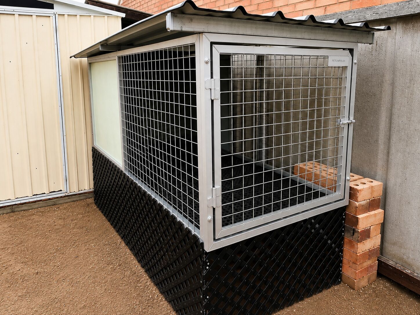 Een metalen hok met een rasterdeur, een ventilatiesysteem en een fundering van bakstenen.