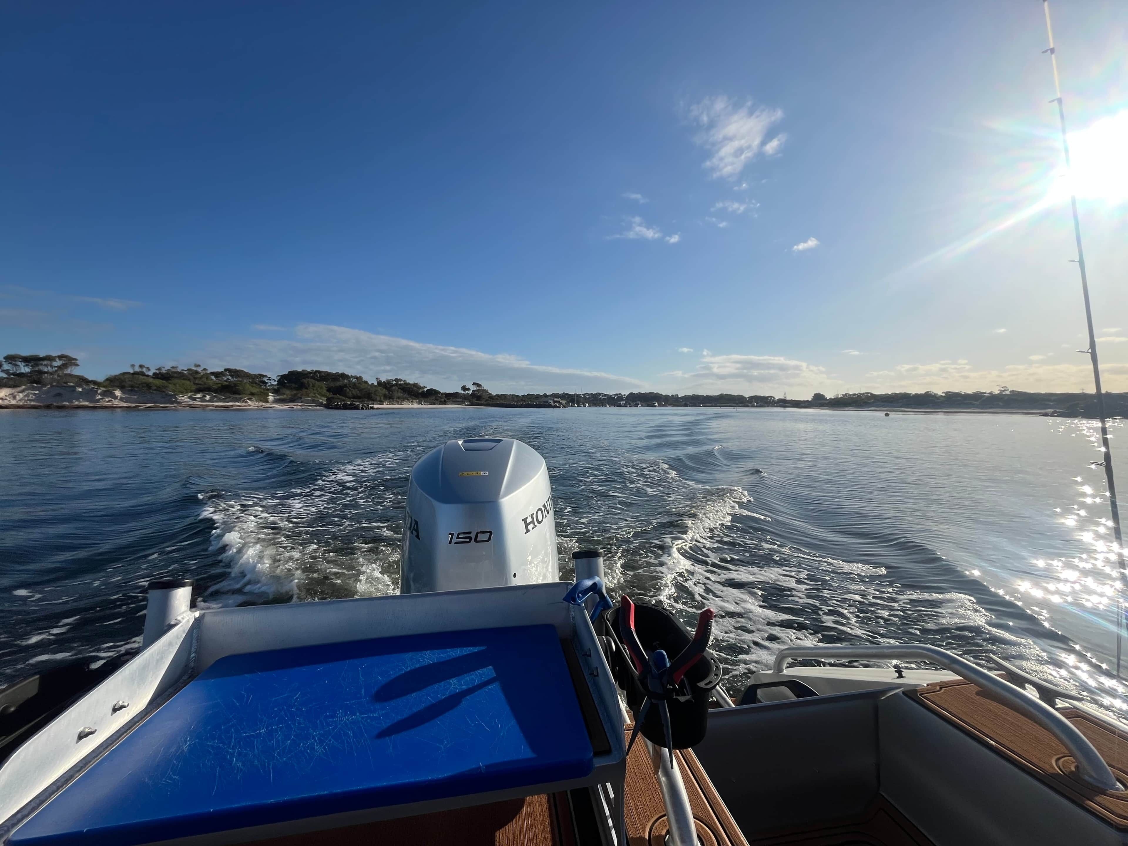A boat's motor and wake on a calm body of water with a clear sky.
