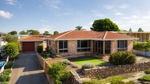 Une maison à deux étages, avec un toit en tuiles, une cour avant avec une pelouse et un mur de soutènement en pierre.