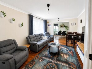 A modern living room with a grey sofa, a coffee table, and a dining area with wooden chairs and a table.