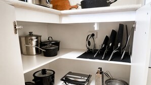Une cuisine avec un plan de travail blanc, une casserole noire, une marmite en acier inoxydable, un autocuiseur noir, une râpe et une passoire.