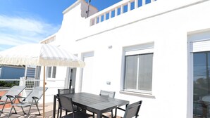 Un patio con una mesa y sillas, un paraguas a rayas y un edificio blanco con un balcón.