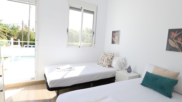 Habitación de hotel con dos camas, un ventanal grande, vistas al exterior y una mesita con lámpara.