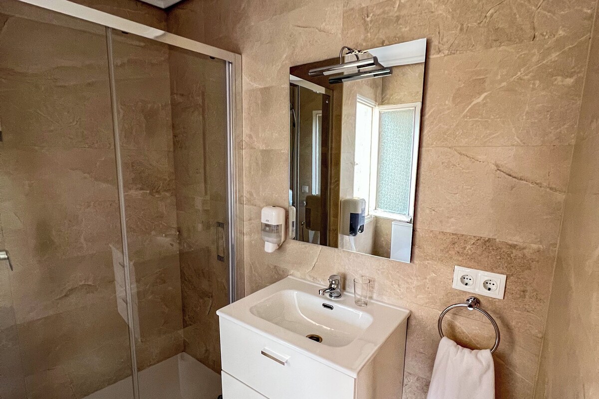 A bathroom with a glass shower enclosure, a white sink with a mirror above it, and a towel ring on the wall.