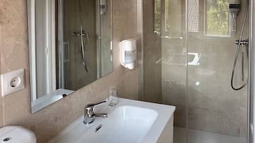 Un baño moderno con un espejo grande, un lavamanos blanco, un cabezal de ducha de mano y una ducha con mampara de vidrio.