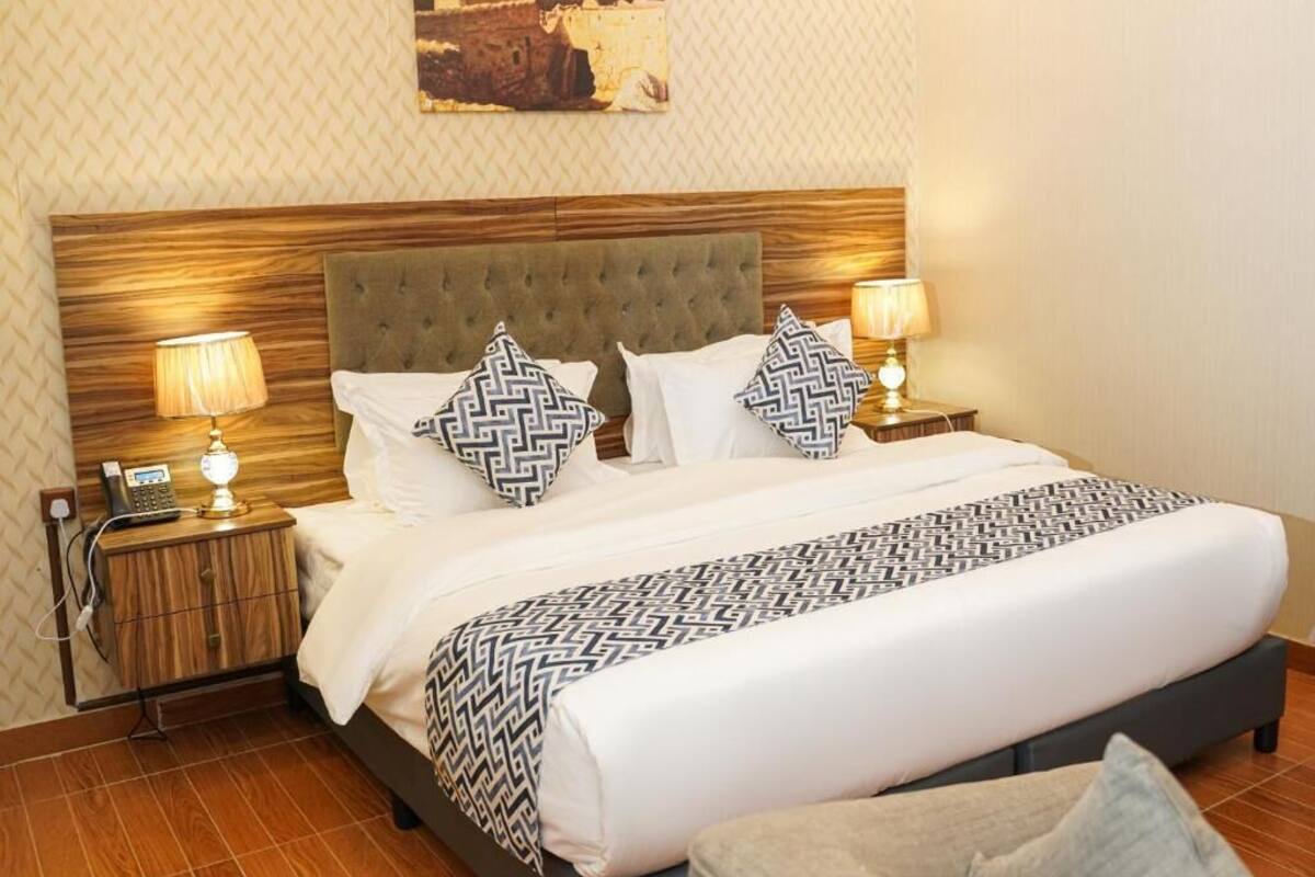 Un lit bien fait, avec une couvre-lit à motifs, deux lampes de chevet et une tête de lit en bois.