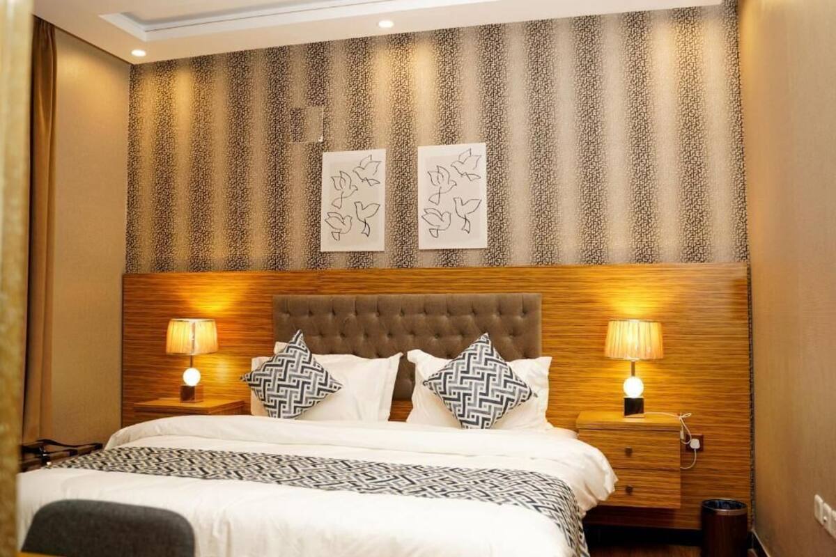 Une chambre d’hôtel avec un grand lit, deux tables de chevet et un mur recouvert d’un papier peint à motifs verticaux.