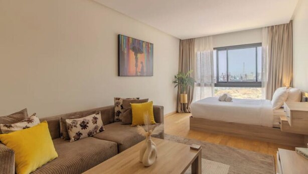 A modern hotel room with a large bed, a sofa, a coffee table, and a painting on the wall.