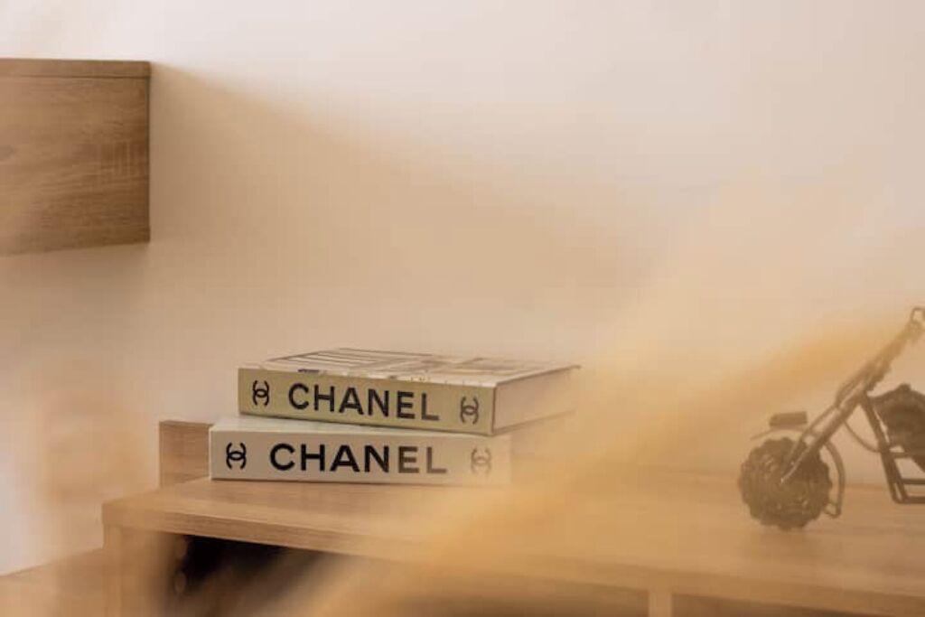 A stack of books with the word "CHANEL" on the cover, placed on a wooden surface next to a wall.