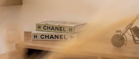 A stack of books with the word "CHANEL" on the cover, placed on a wooden surface next to a wall.