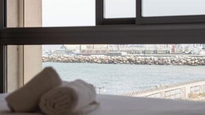 A window view of a rocky waterfront with a bridge, a building in the background, and a rolled towel on a surface.