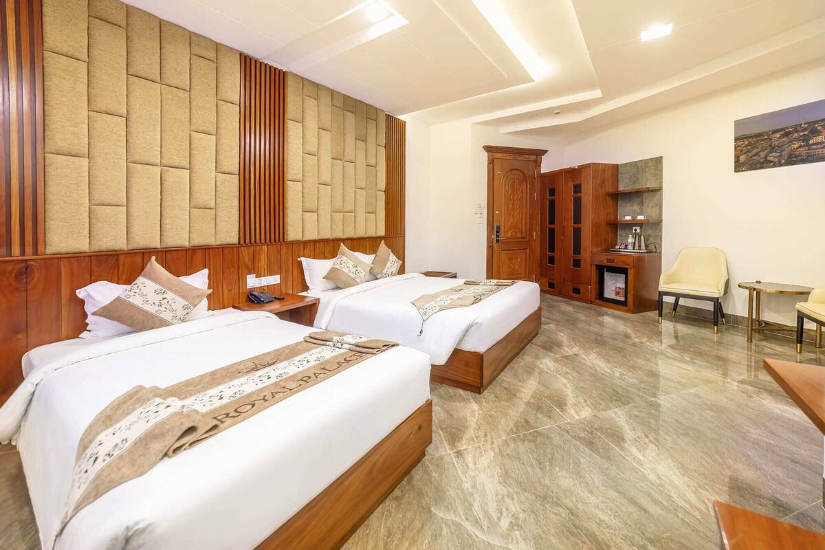 A hotel room with two beds, a wooden headboard, a minibar, a seating area, and a painting on the wall.
