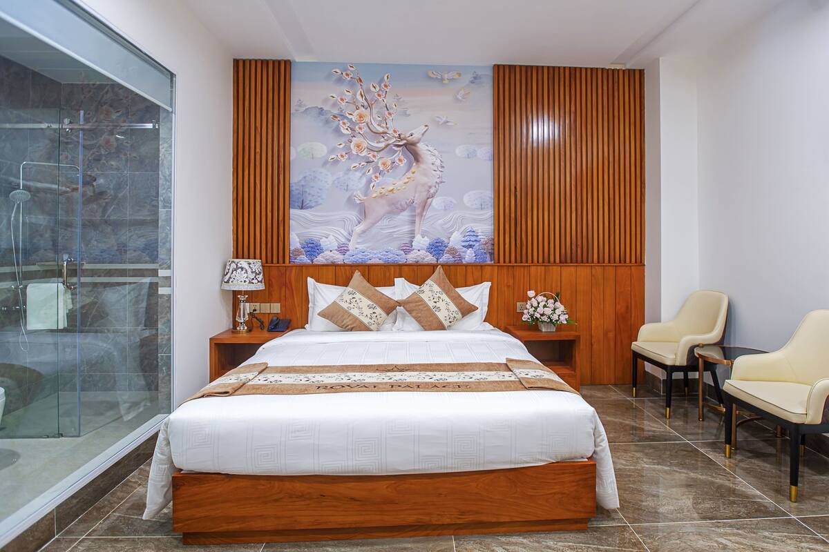 A hotel room with a large bed, a wooden headboard, a glass shower enclosure, and a mural on the wall.