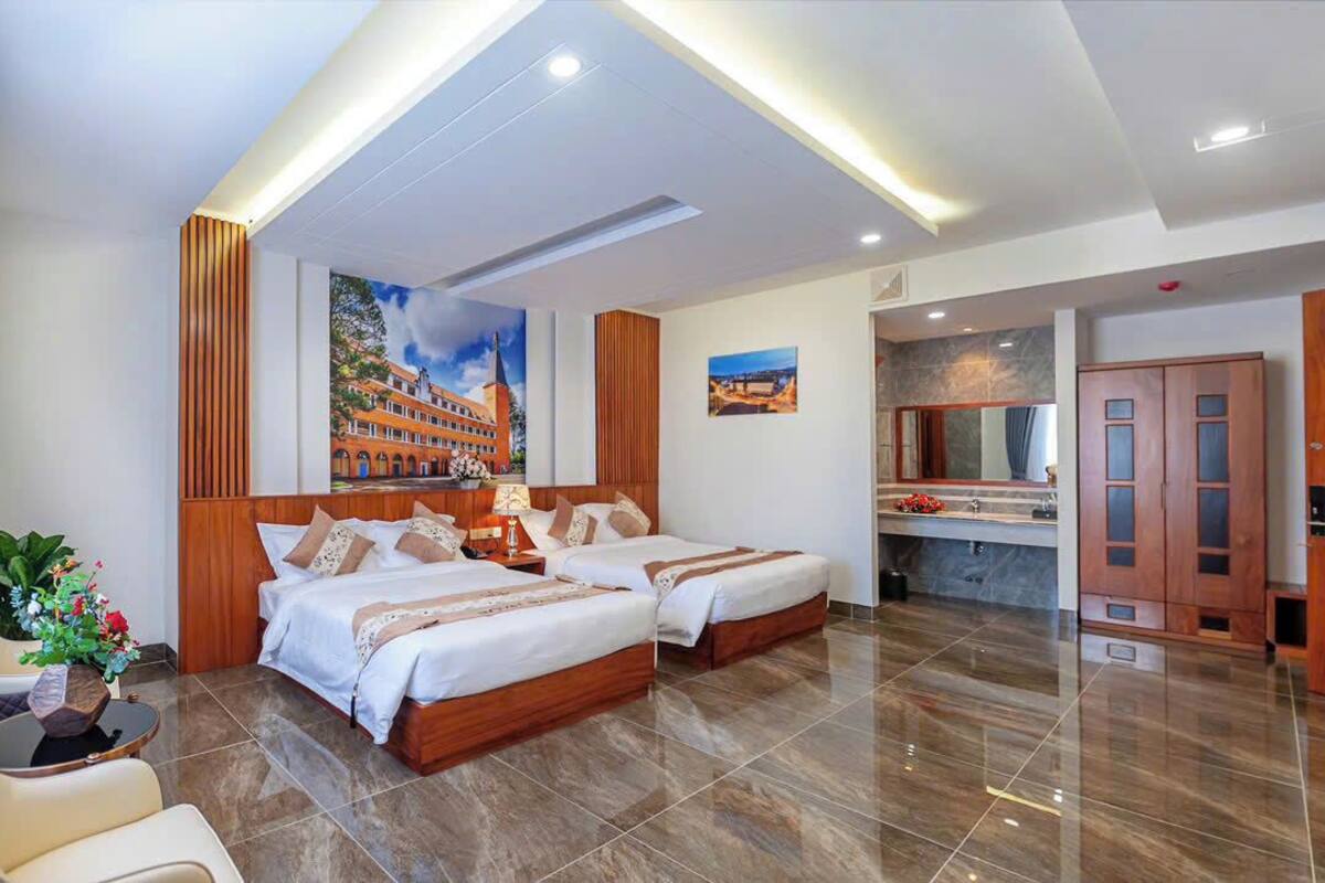 A hotel room with two beds, a sitting area with a chair and table, a bathroom with a mirror and sink, and a dining area with a counter.