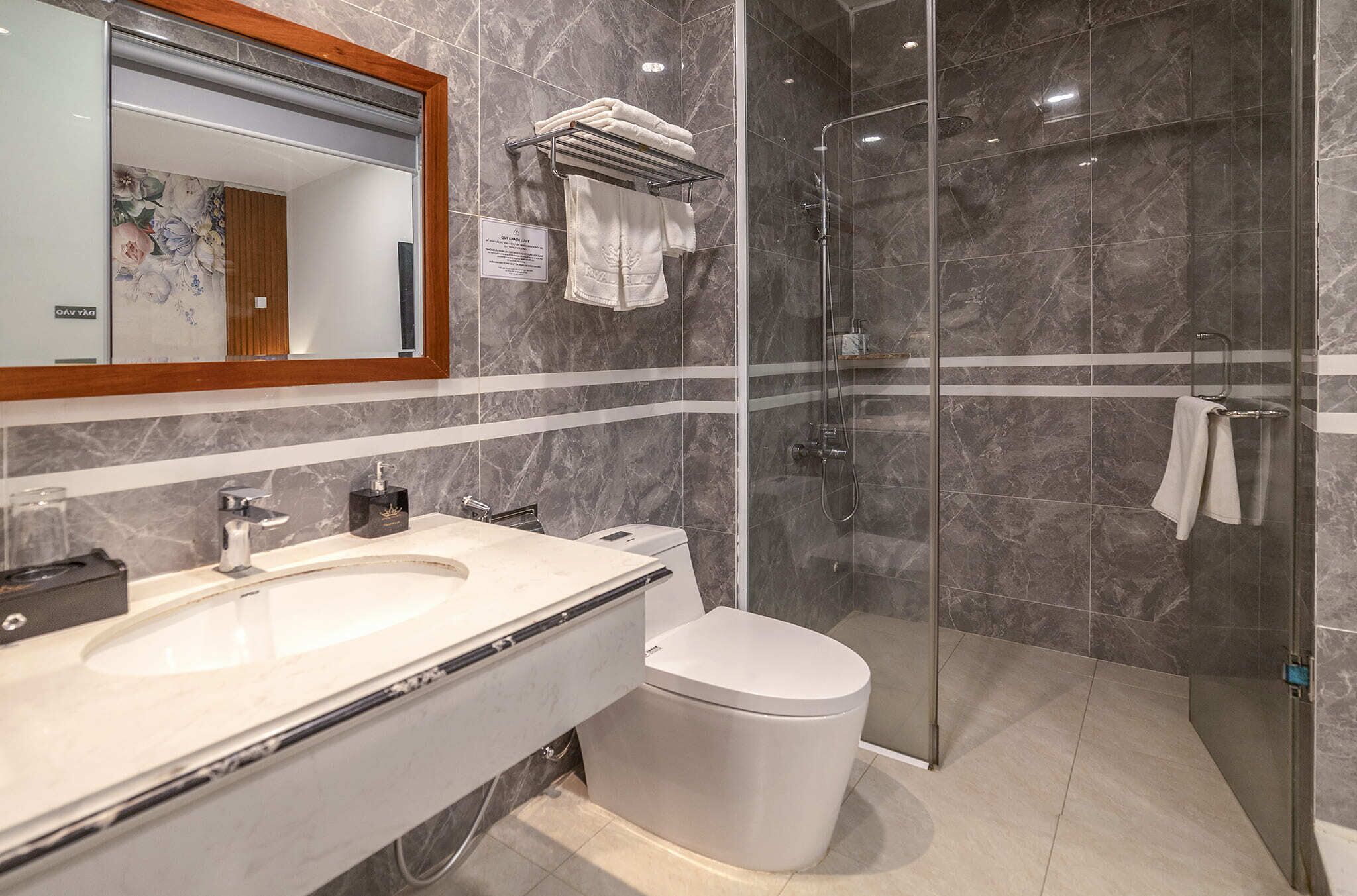 A modern bathroom with a large mirror, two sinks, a toilet, and a glass-enclosed shower area.
