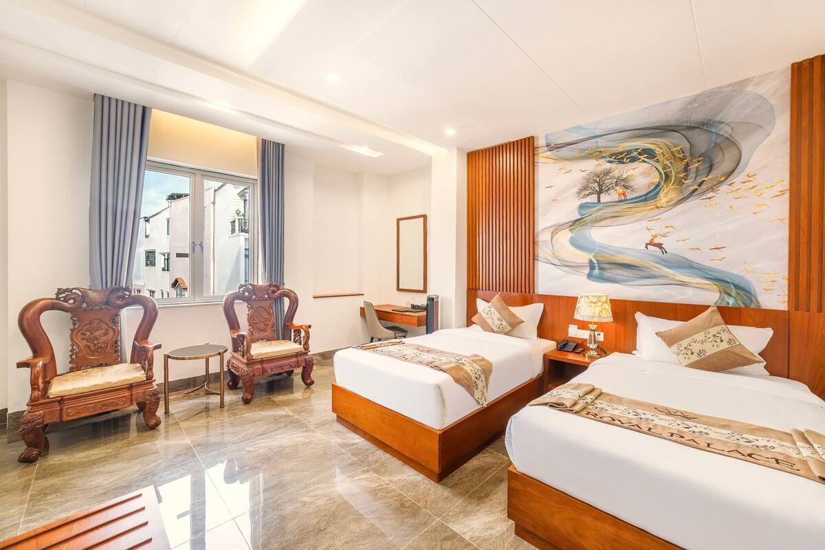 A hotel room with two beds, a desk, a chair, and a large window.
