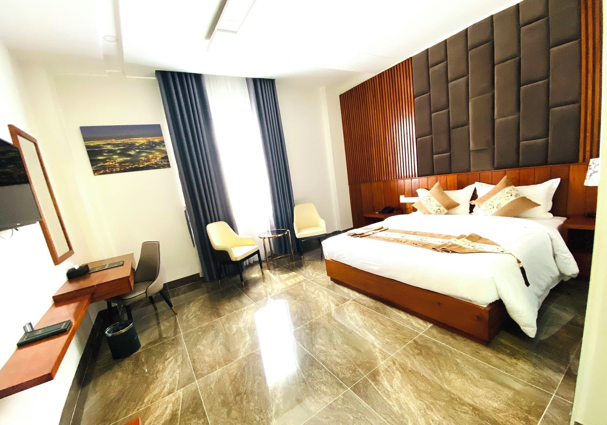 A hotel room with a large bed, a desk with a chair, a small table, and a TV.