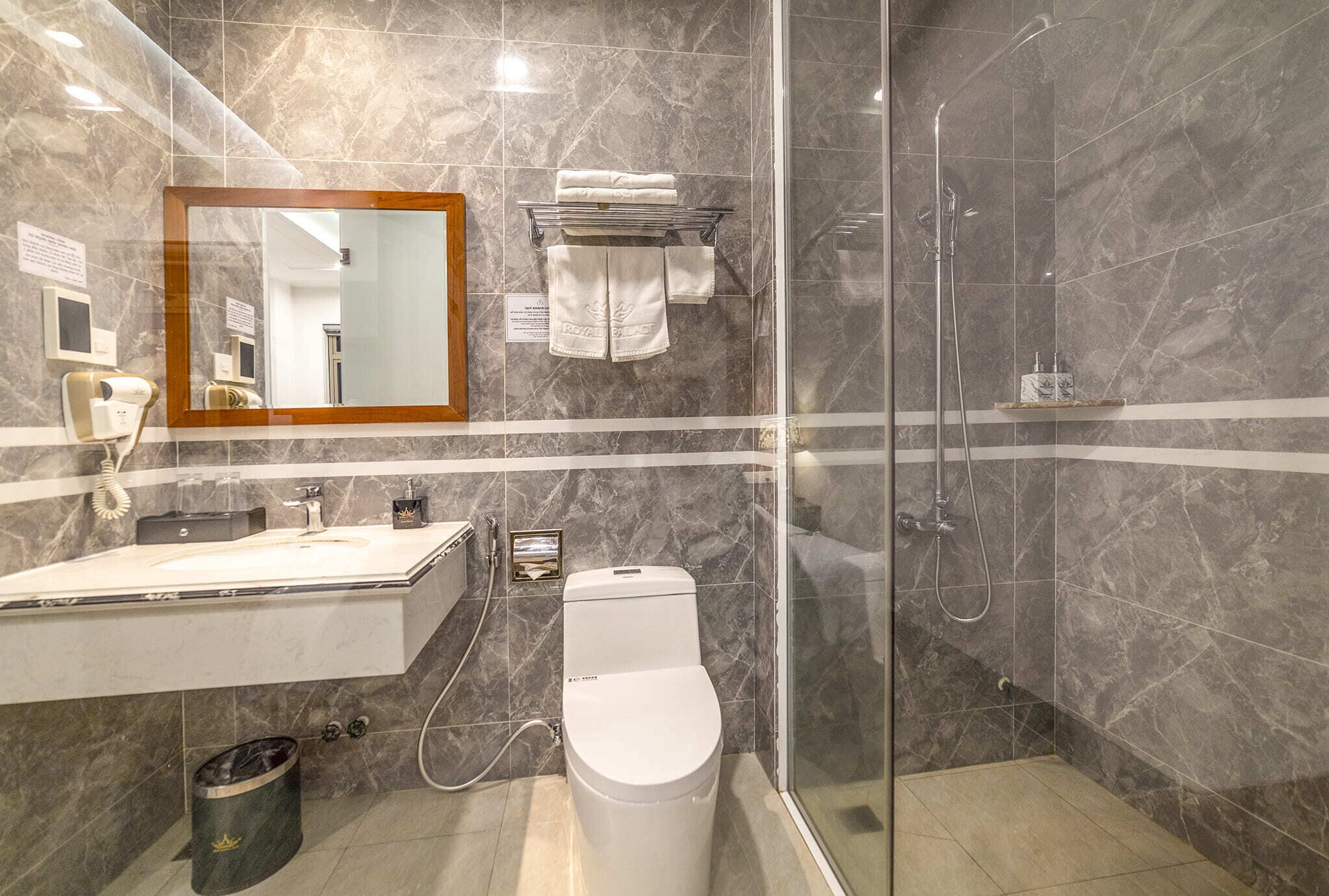 A modern bathroom with a marble sink, a toilet, a glass-enclosed shower, and a mirror with a wooden frame.