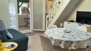 A cozy living area with a sofa, a dining table with a floral tablecloth, a TV on a stand, and a staircase leading to an outdoor area. - St Cyprien: The art of seaside living (Saint-Cyprien)