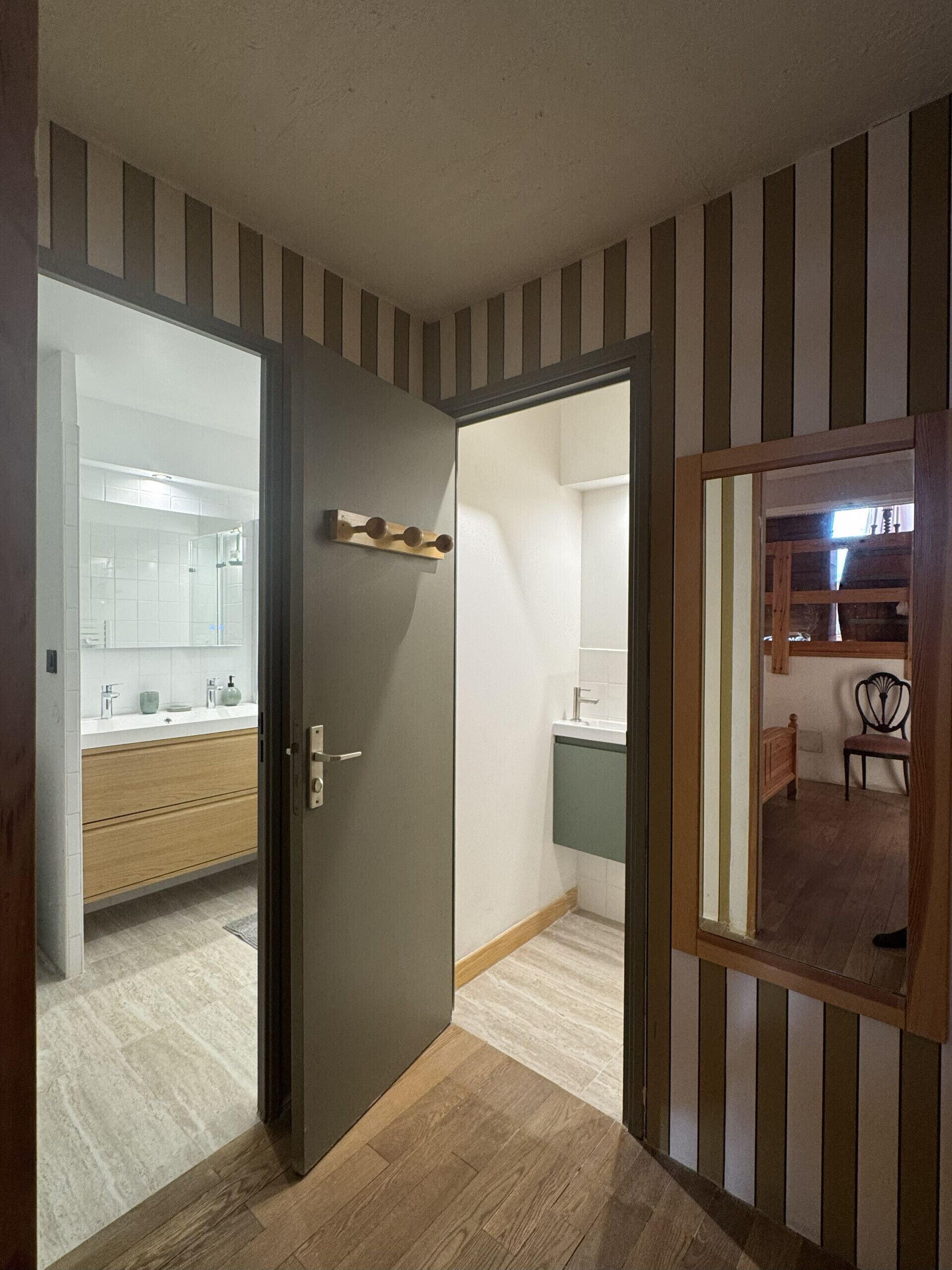 A hallway with striped walls, a wooden door, and a view into a bathroom with a white sink and mirror.