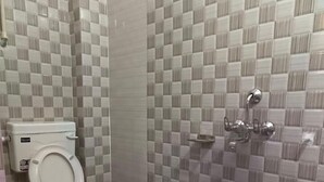 A bathroom with a toilet, a shower, and a blue bucket. - Maa Vaishnavi guest house (Varanasi)