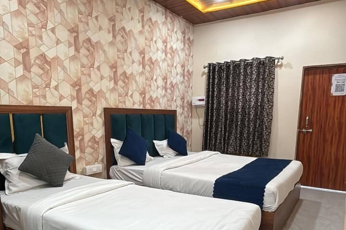 Quarto de hotel com duas camas, cabeceiras de madeira, papel de parede estampado, um ventilador de teto e uma porta com código QR.