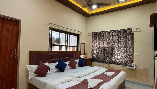 A bedroom with a large bed, wooden headboard, ceiling lights, a ceiling fan, and a window with curtains. - Maa Vaishnavi guest house (Varanasi)