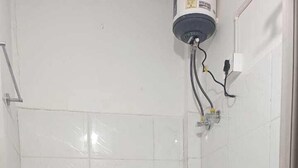 A small, tiled bathroom with a toilet, shower, and a blue bucket. - Vinayaka Inn Sittong (Kurseong)