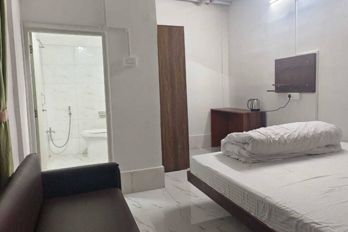 A hotel room with a bed, a wooden cabinet, a wall-mounted TV, and a shower area.