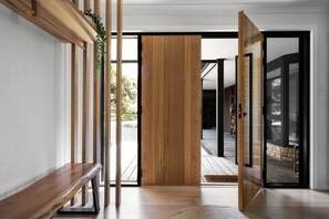 Een modern interieur met een houten bankje, een schuifdeur naar een buitenruimte en uitzicht op de omgeving.