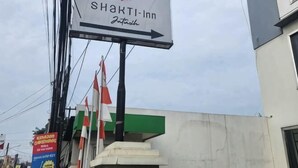 Une enseigne pour le Shakti Inn, avec une flèche indiquant la direction, plusieurs drapeaux et la façade du bâtiment.