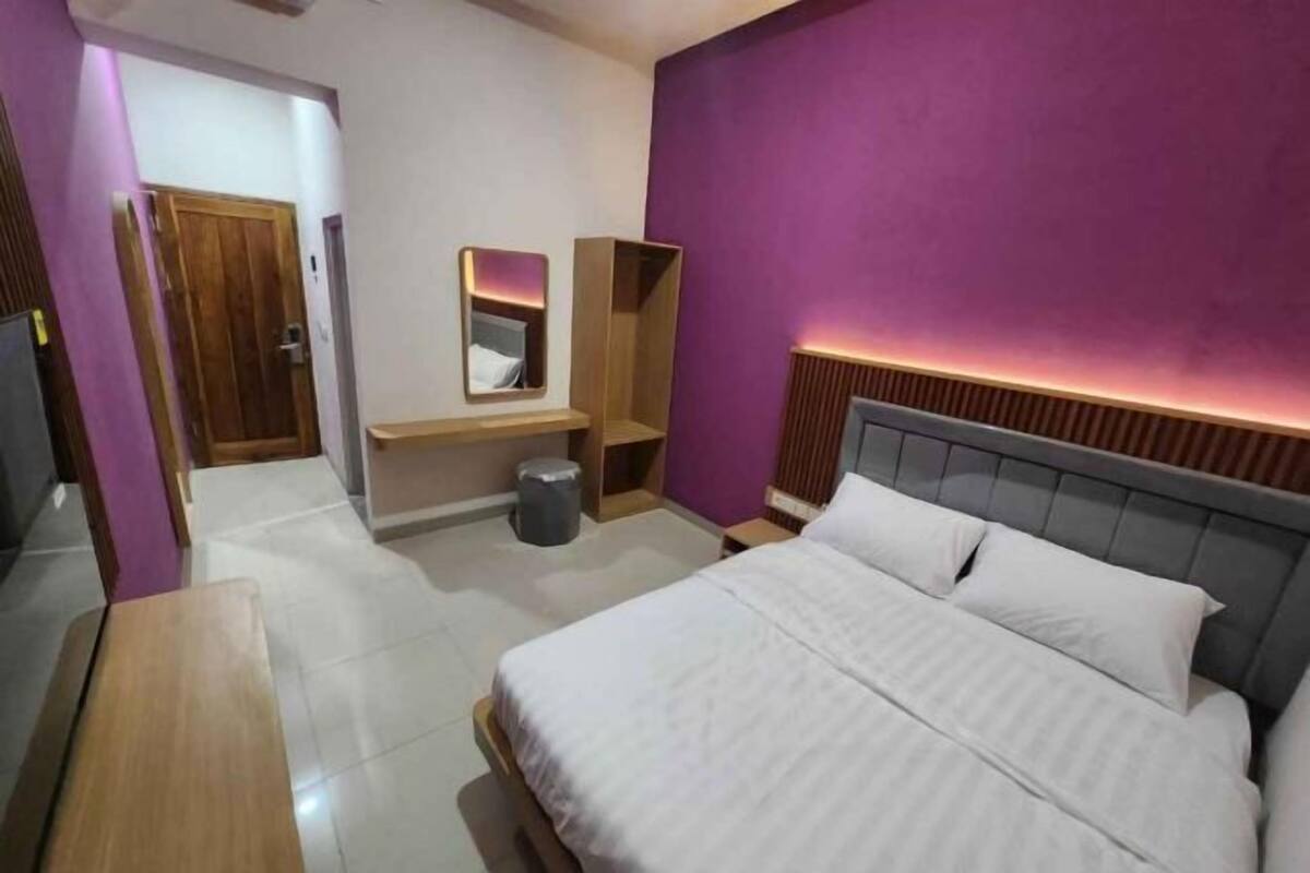 A bedroom with a bed, a bedside table, a mirror, a wooden wardrobe, and a trash bin.