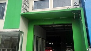L’entrée d’un immeuble est surmontée d’un auvent vert, on aperçoit une porte de garage et une voiture rouge à l’intérieur.