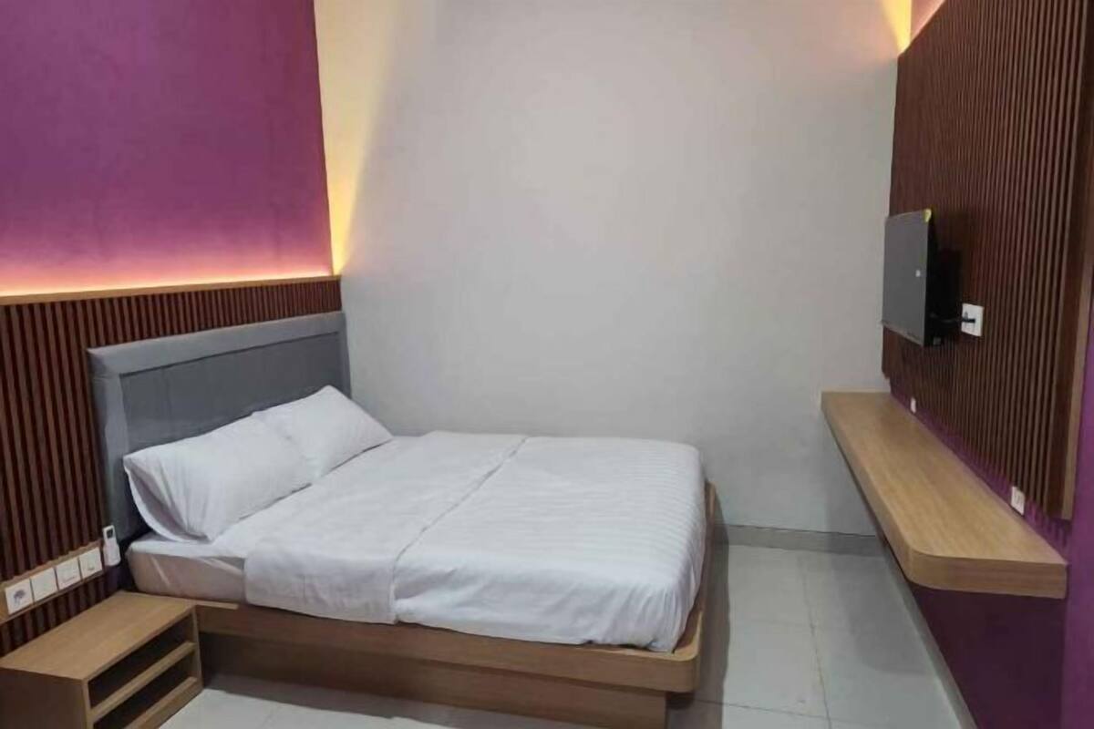 A single bed with a wooden frame, a bedside table, and a wall-mounted TV.
