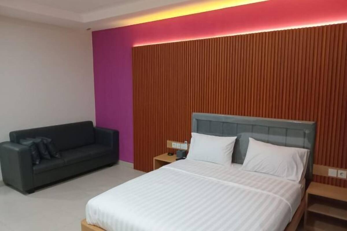 A hotel room with a bed, a nightstand, a bedside table, a sofa, and a wall with vertical wooden slats.