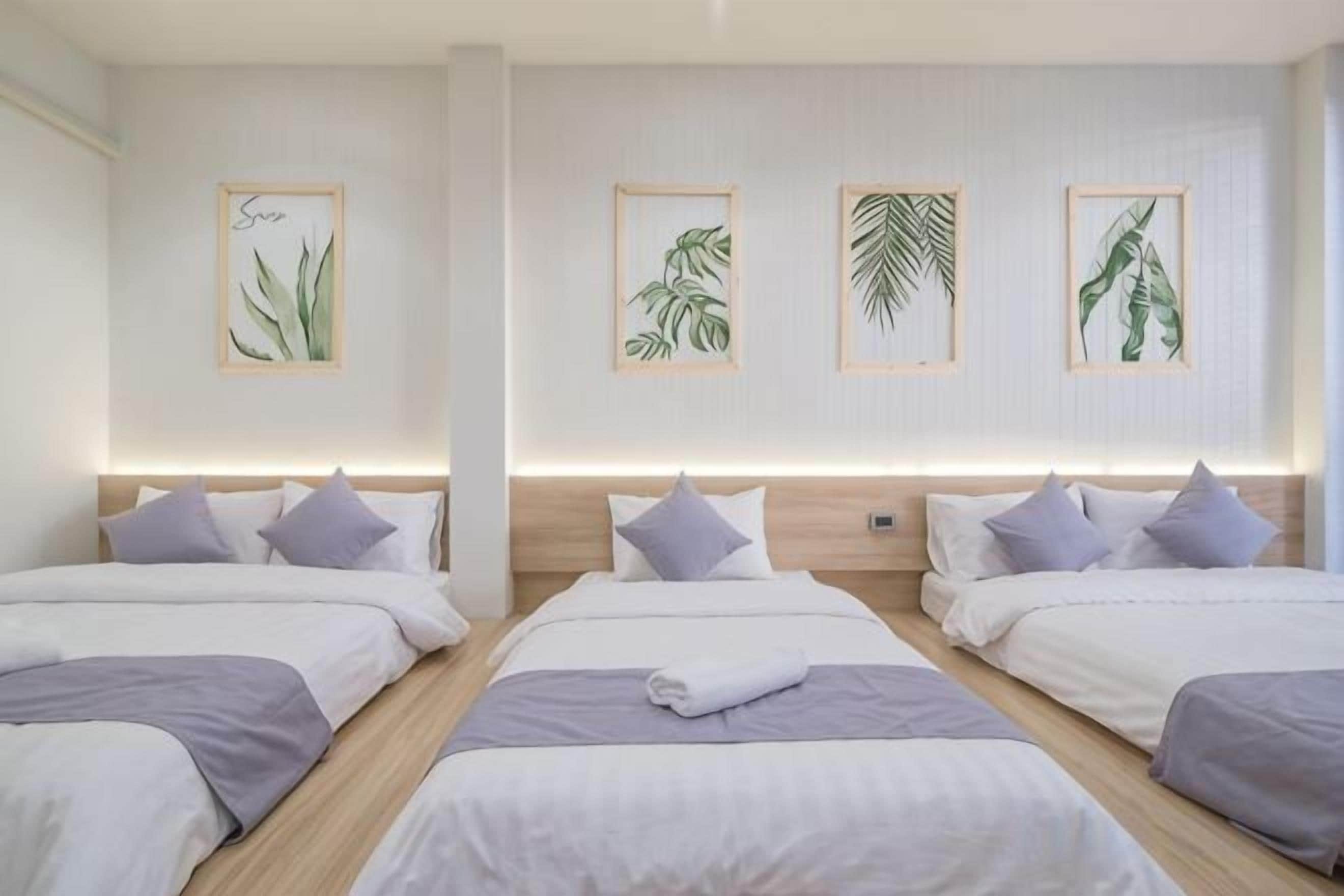 A hotel room with four beds arranged in a row, each with a headboard and pillows.