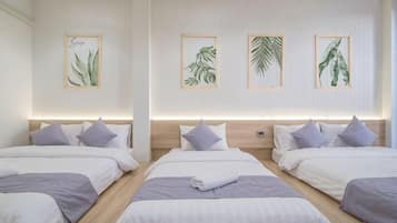 A hotel room with four beds arranged in a row, each with a headboard and pillows.