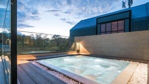 Jacuzzi en la azotea con terraza de madera y guijarros, rodeado por una barandilla de vidrio y un edificio moderno.
