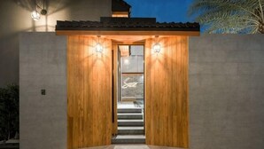 Una entrada de madera con una escalera que conduce al interior, un muro de concreto y una lámpara sobre la puerta.