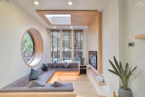 Una sala de estar moderna con un sofá modular, un ventanal redondo y un televisor de pantalla plana.