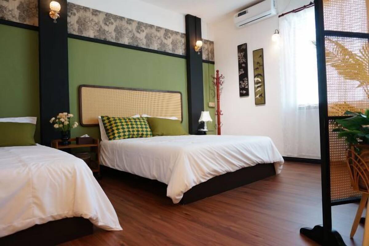 A hotel room with two beds, a green accent wall, a wooden floor, and a window with a view.