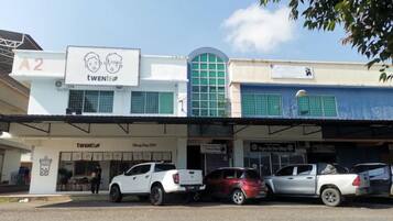 A building with a sign 'A2' and 'TWENI' on the facade, a parking area with several cars, and a visible storefront with a sign 'Barber Shop'.