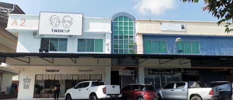 A building with a sign 'A2' and 'TWENI' on the facade, a parking area with several cars, and a visible storefront with a sign 'Barber Shop'.