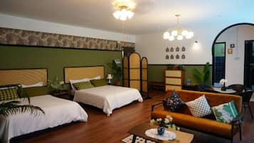 A hotel room with two beds, a sofa, a dining table, and a decorative plant.