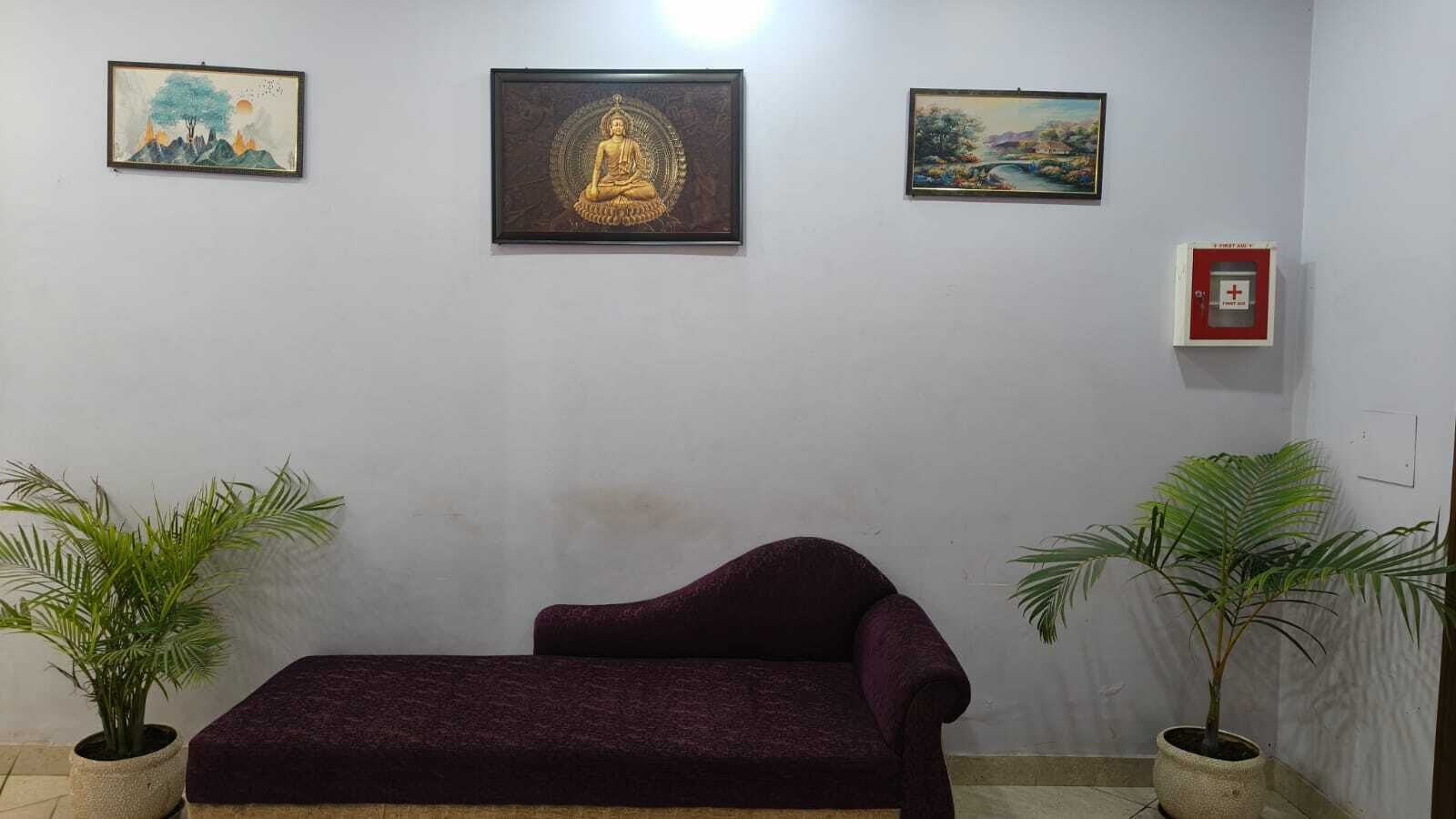 Una habitación con un sofá color púrpura oscuro, dos plantas en macetas y tres cuadros en la pared.