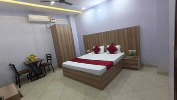 A bedroom with a bed, bedside tables, a desk with chairs, and an air conditioning unit.