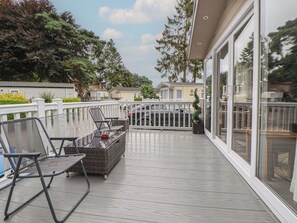 A covered outdoor deck with wicker furniture and a glass door leading to a covered area. - Delta Superior (Ruthin)