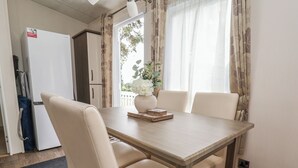 Ein Essbereich mit einem Holztisch, zwei weißen Stühlen, einer Blumenvase und einem weißen Kühlschrank im Hintergrund.
