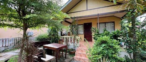 A house with a porch, a table, and chairs, surrounded by various plants and trees.